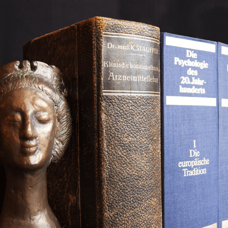 Escultura clássica ao lado de livros antigos de psicanálise e medicina, em ambiente de estudo. Escuta psicanalítica – Juliana Bucher.
